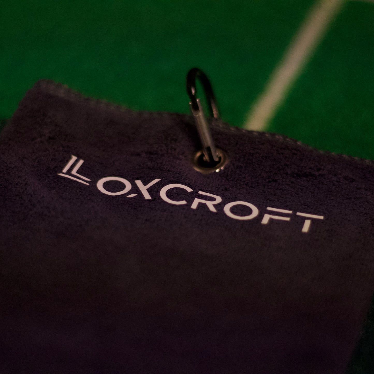 A light gray golf towel hanging on a golf bag, showcasing its soft texture and practical design, perfect for keeping clubs and hands clean during a game.