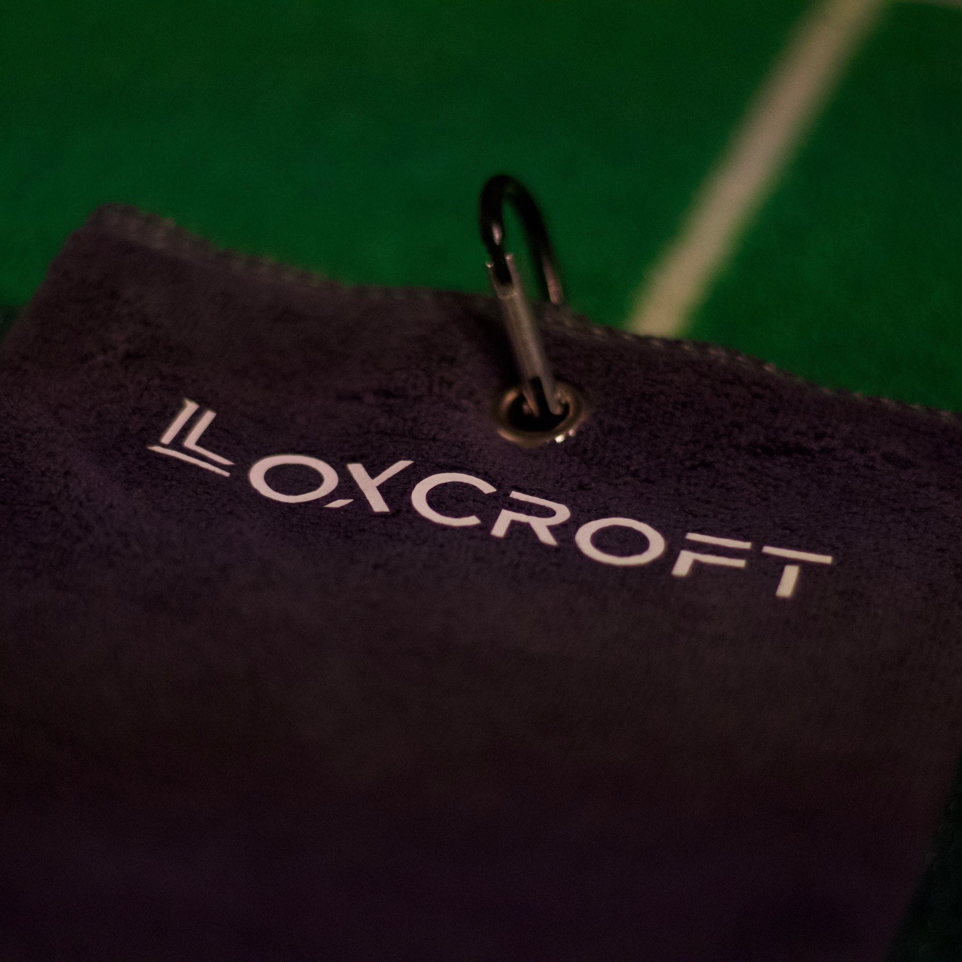 A light gray golf towel hanging on a golf bag, showcasing its soft texture and practical design, perfect for keeping clubs and hands clean during a game.